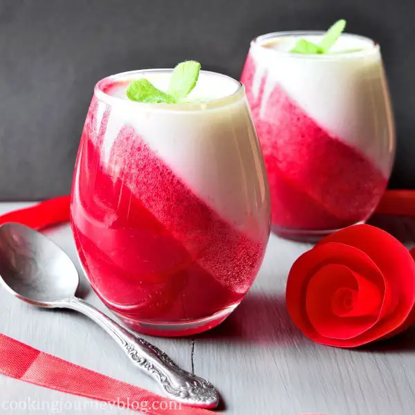 Easy strawberry desserts in glasses with red and white layers, served on grey table with a teaspoon and rose.
