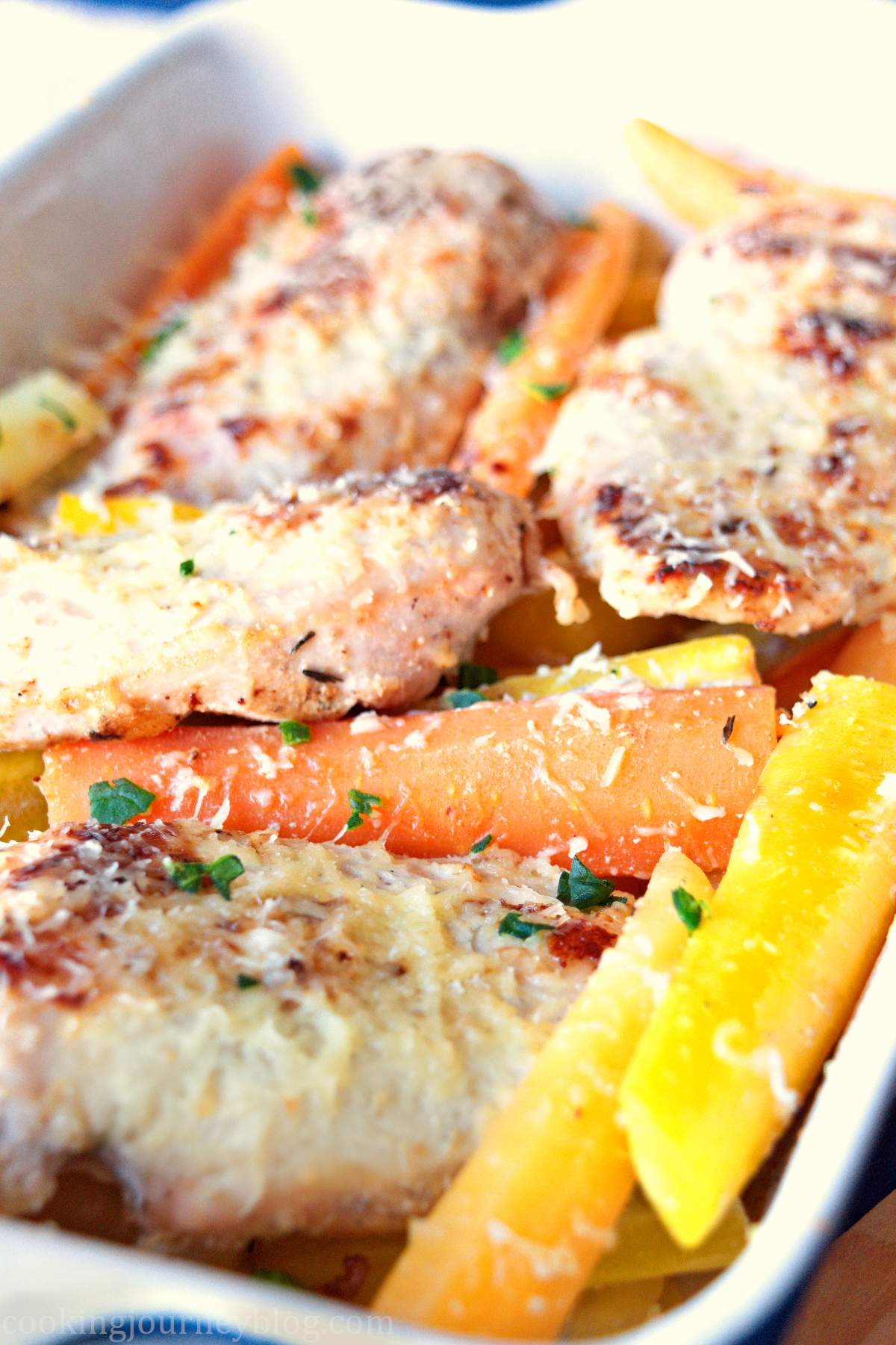 Baked chicken breasts and roasted baby carrots in a baking dish, served on a blue table