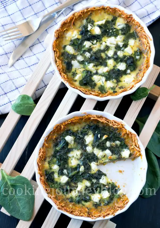 Spinach quiche, served on wooden board on the black table. One slice is missing.