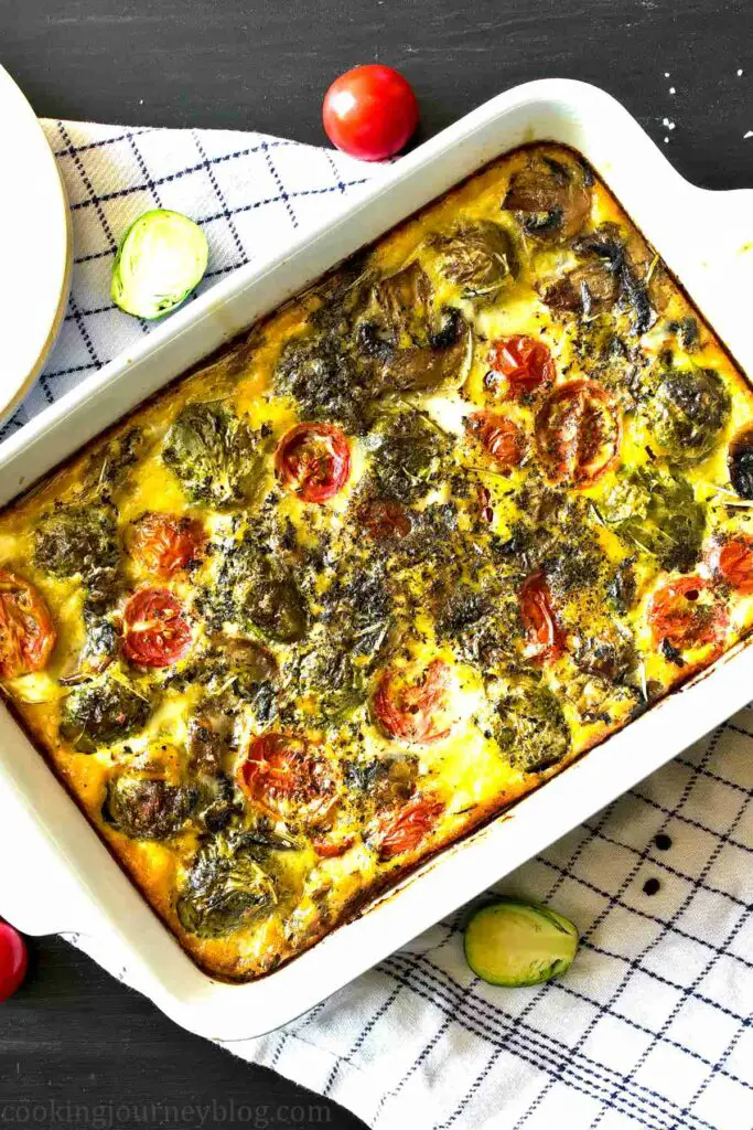 Breakfast frittata with mushrooms, Brussels sprouts and tomatoes, served on a black table in baking dish