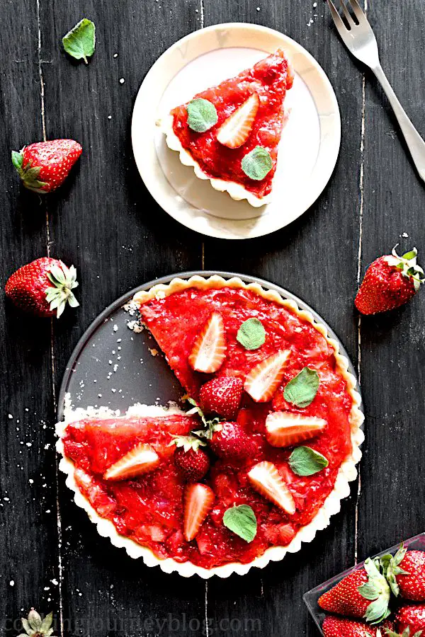 Strawberry tart and its slice on a plate, served on a black table