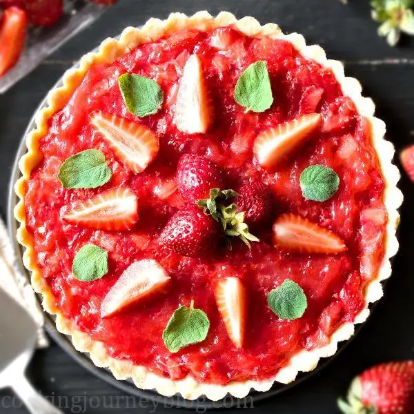 Red strawberry tart, topped with fresh strawberries and mint leaves, served on black table