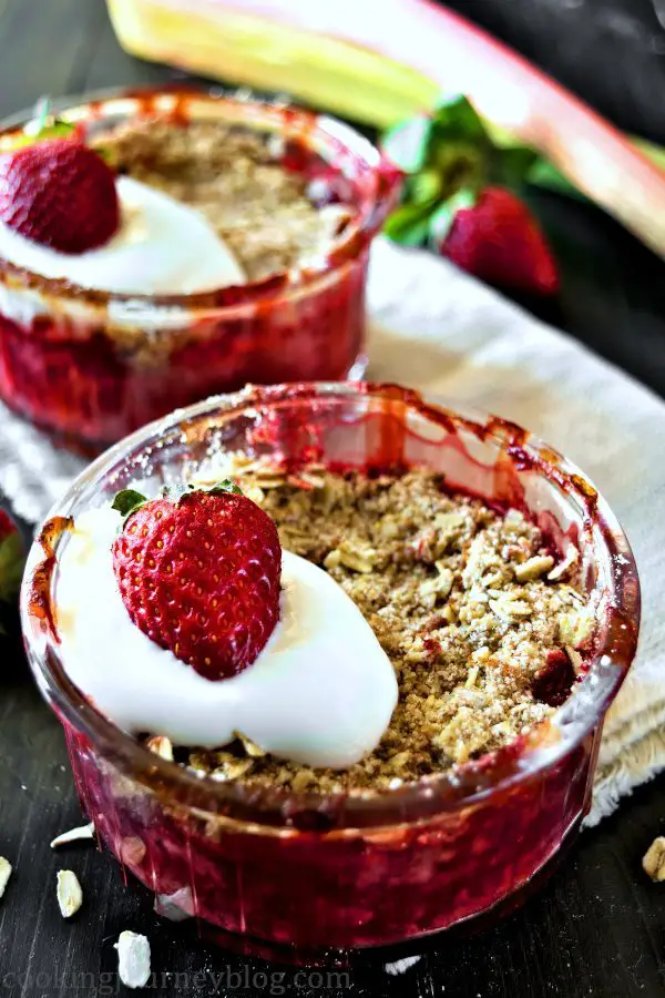 Strawberry rhubarb dessert, served with yogurt and strawberries in individual ramekins on a black table.