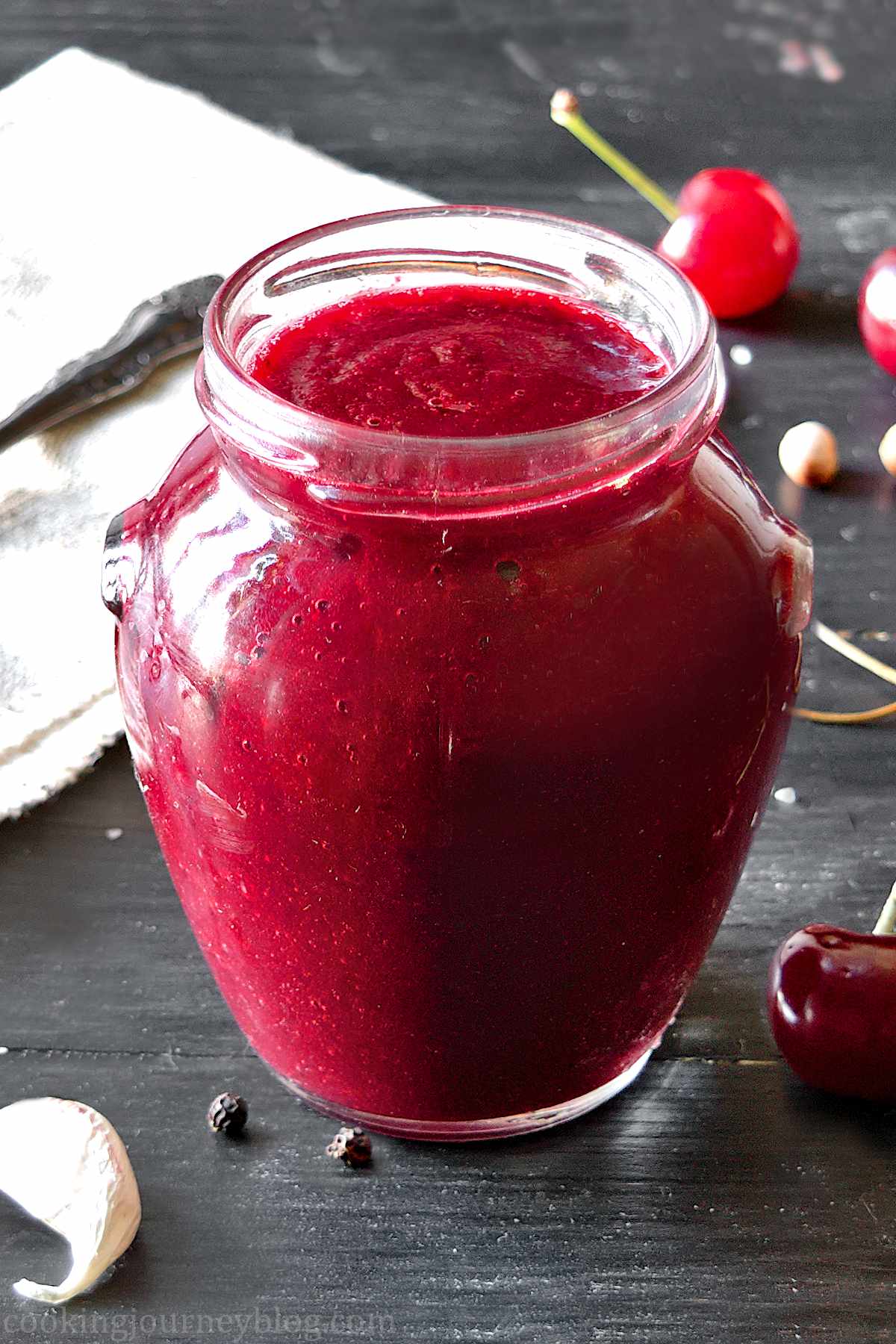 Savory cherry sauce in a jar with fresh cherries on the black table