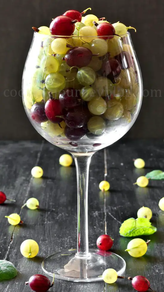 Green and red gooseberries in a wine glass on a black table