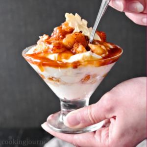 Holding caramel apple trifle with dried apple slice in hands with a spoon