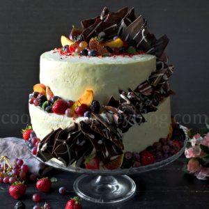 Peach Cake with Cream Cheese Frosting – 2 Tier Cake on a black table, with fruits on a cake stand