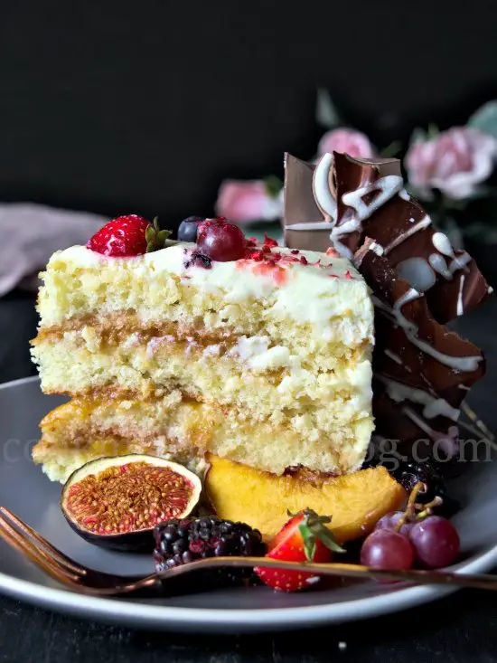 Peace of peach cake with Cream Cheese Frosting, chocolate and fruits. Placed on grey plate.