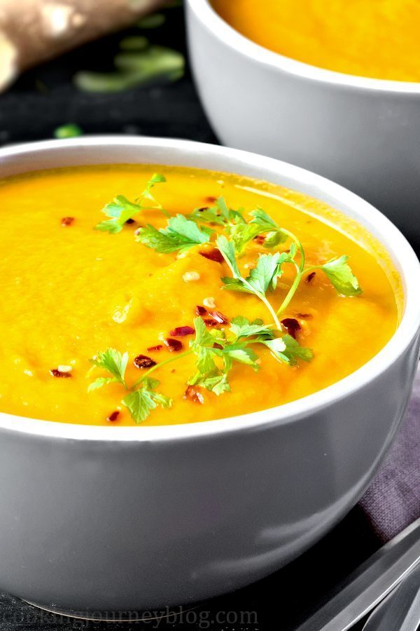 Vegan Carrot Ginger Soup with parsley and chili, in grey bowls on a black table. MAde with healthy immune boosting ingredients.