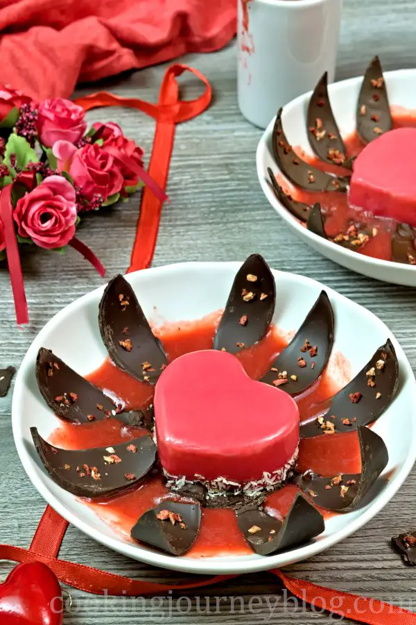 Mirror glaze cake, blooming with chocolate leaves and strawberry sauce on a plate for Valentine's day.