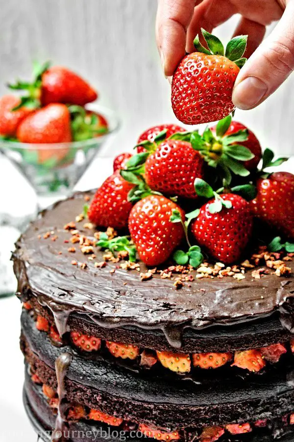 Vegan Chocolate Cake, decorated with strawberries. Served on a white table with red ribbon on the table.
