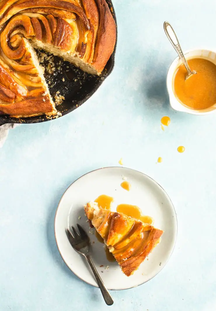 Bourbon Butterscotch Skillet Cinnamon Roll and a slice on a plate, drizzles with glaze