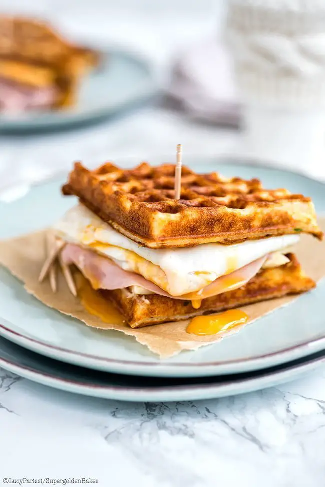 Parmesan waffle sandwich with ham, cheese and egg, served on a white plate