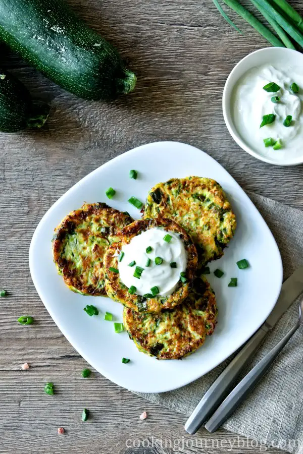 Zucchini fritters on a plate, view from top, served on  a table with green zucchini and scallions