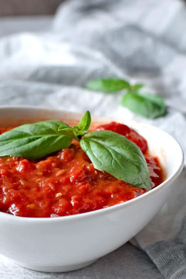 Homemade Marinara Sauce served in a small white plate with fresh basil on top