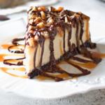 A slice of Turtle Cheesecake with caramel sauce, chocolate sauce and pecans