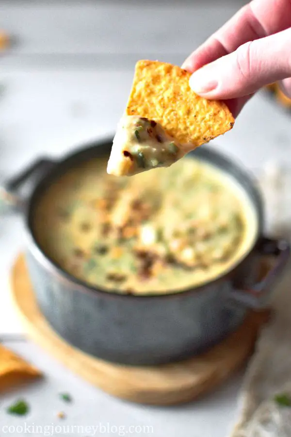 Holding tortilla chips, dipped in Mexican con queso.