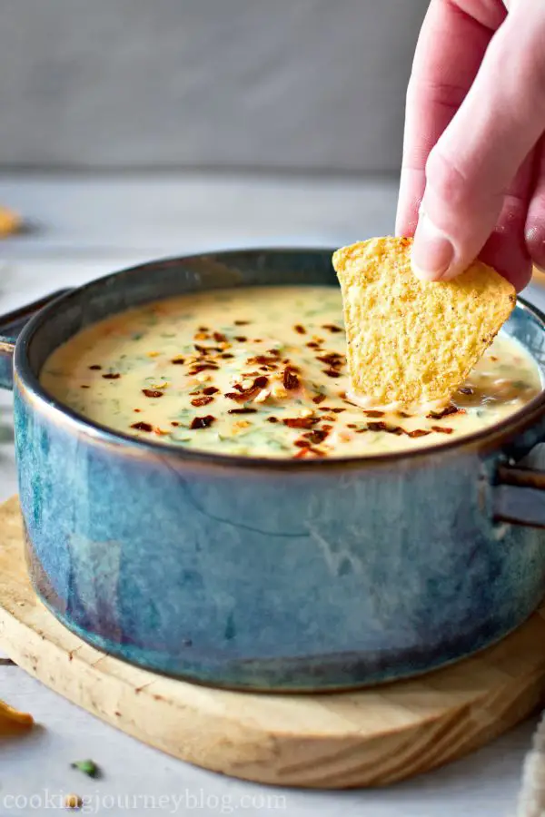 Dipping tortilla chips in chile con queso in a blue bowl