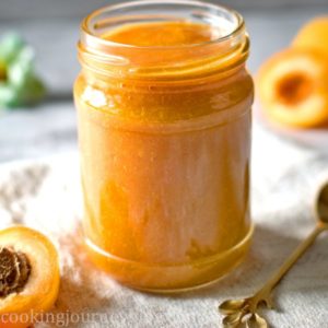 Apricot jam in a glass jar with a golden spoon and apricots on the table