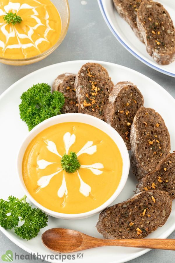 Pumpkin soup served with parsley and sliced bread on a white plate