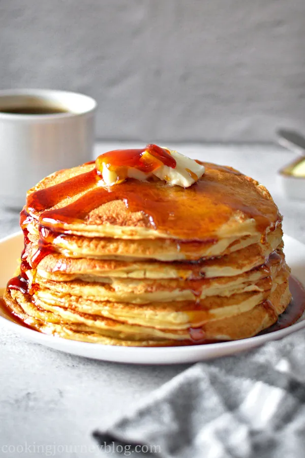 A stack of fluffy buttermilk pancakes served with syrup on the white plate