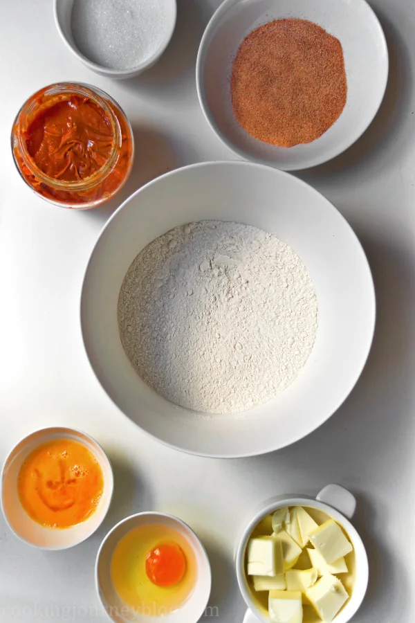 Bowls with ingredients for empanadas dough: sugar, cinnamon sugar, cajeta, flour, an egg, beaten egg and cubed butter.