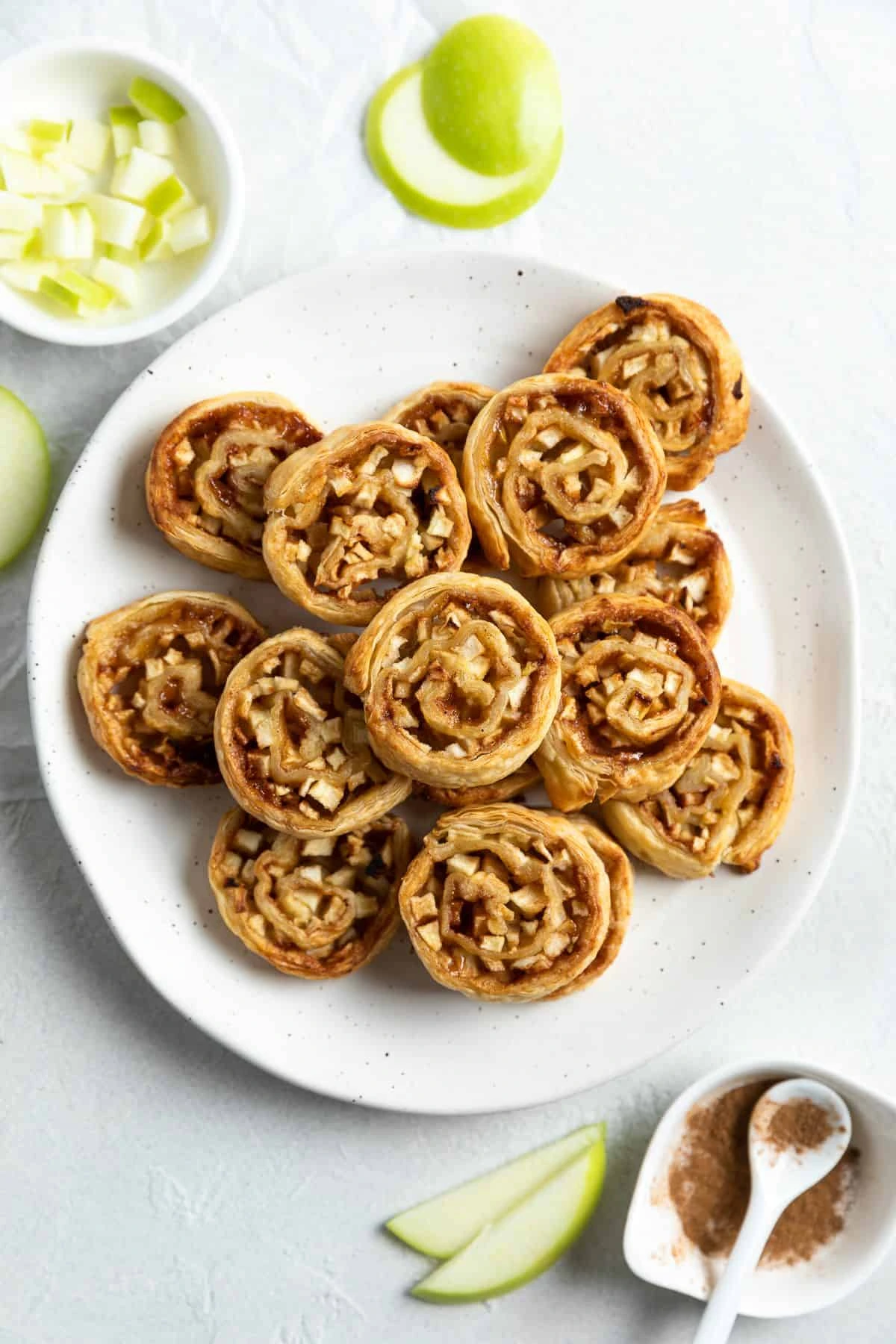 Pinwheels served on a white plate with cinnamon and apple slices.