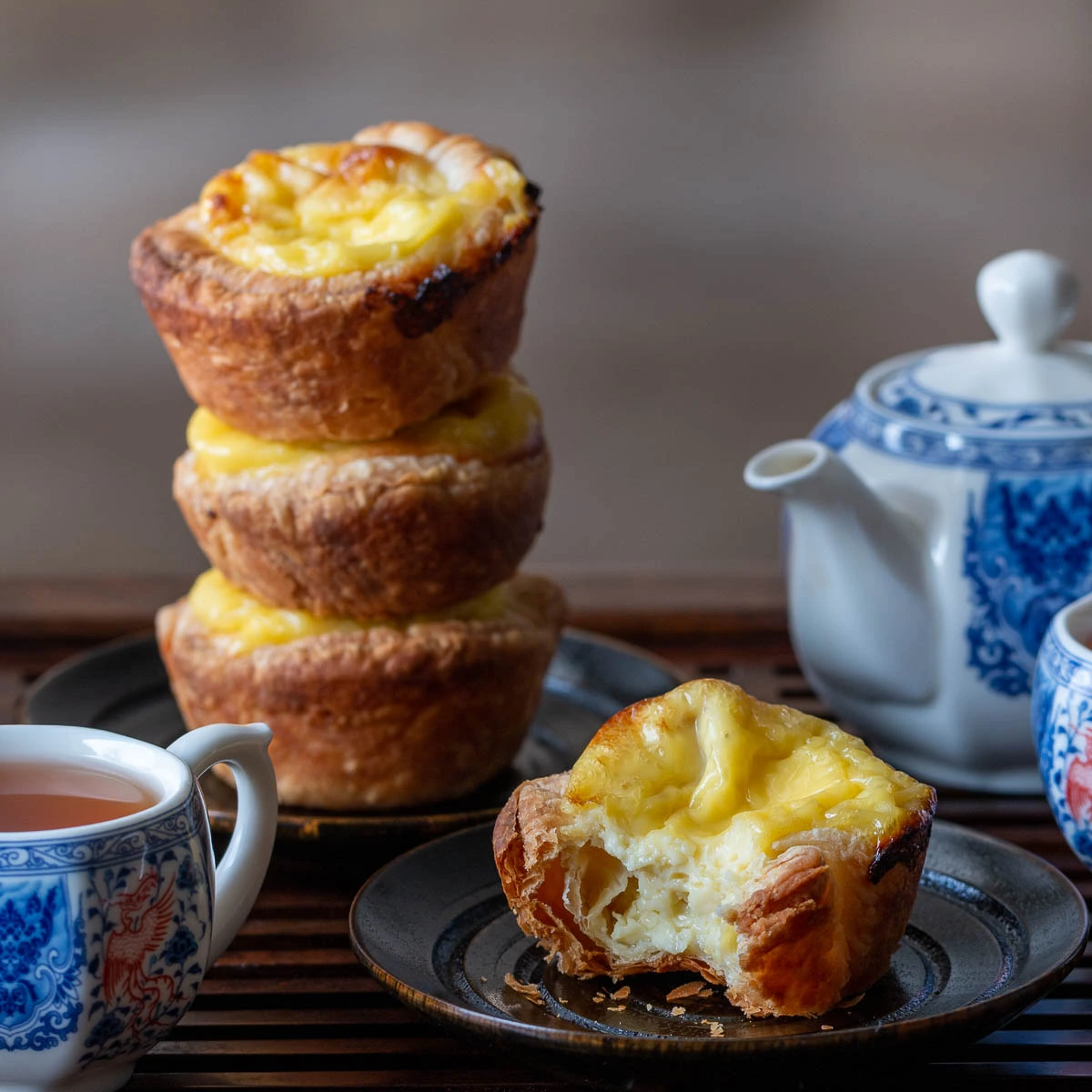 Egg tarts served on a black plate with a teapot and a cup of tea