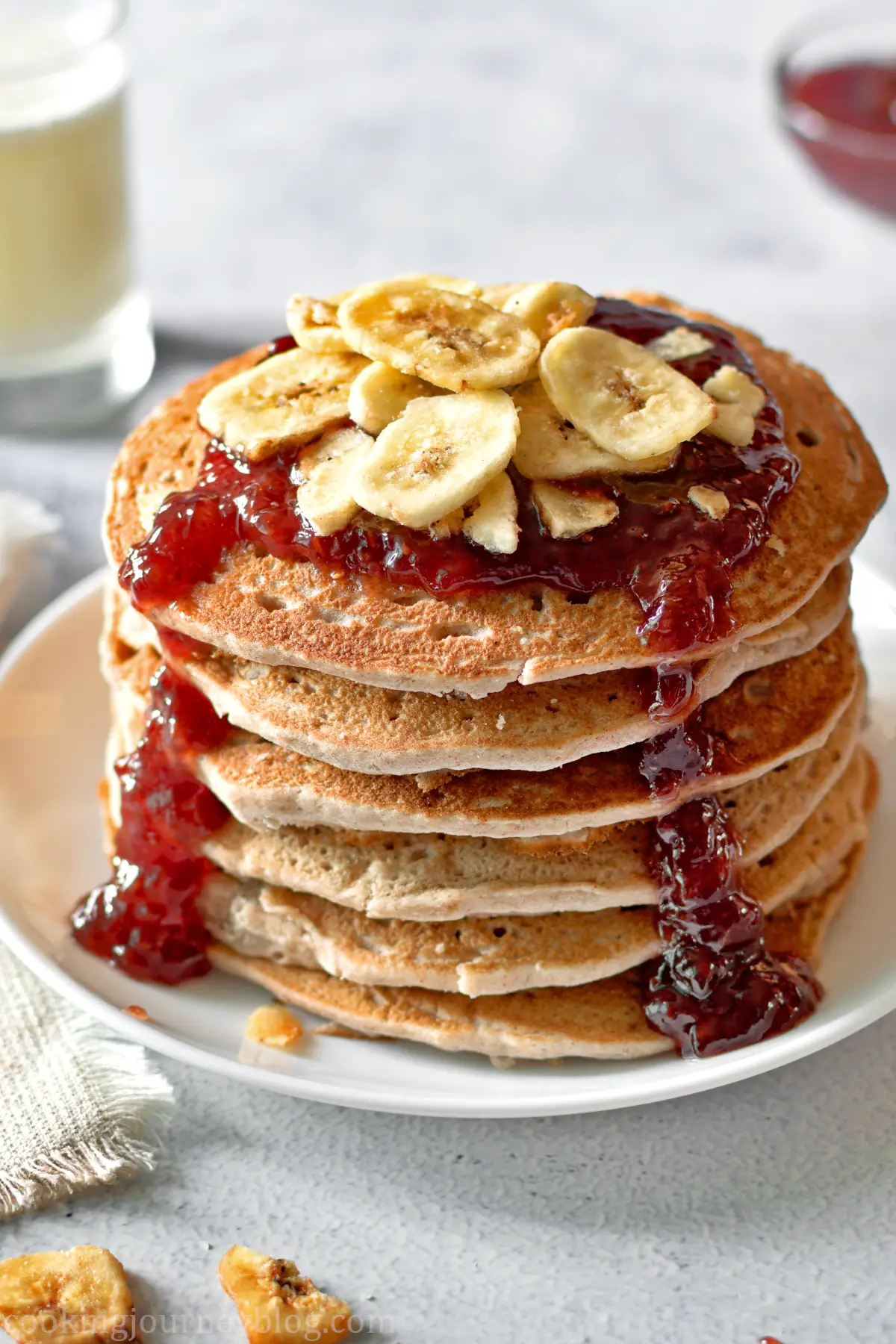 Banana Buckwheat Pancakes served with red jam and bananas on a white plate