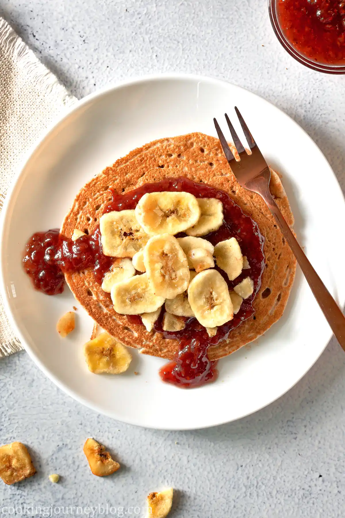 Banana Buckwheat Pancakes served with jam and bananas on a white plate with a fork