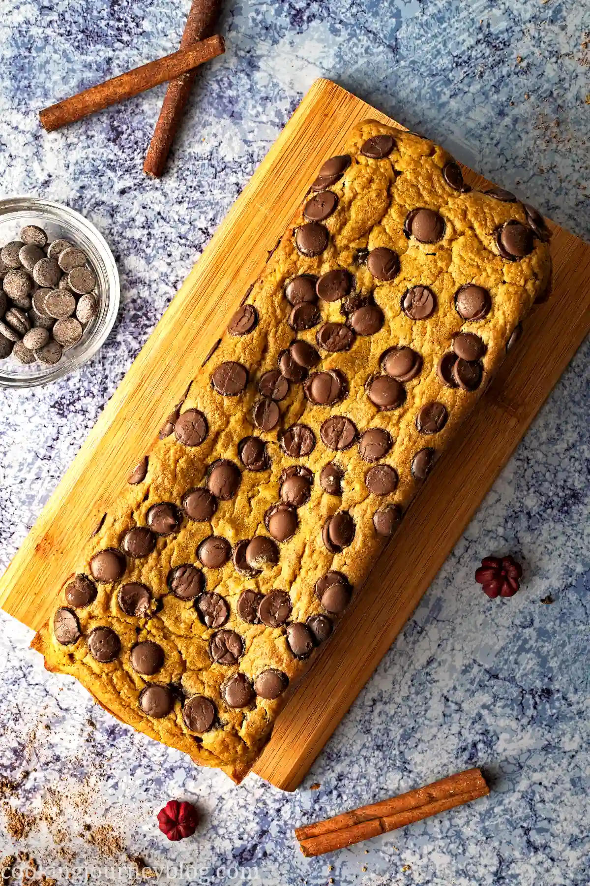 Pumpkin chocolate chip bread, view from top, served with chocolate chips and cinnamon sticks on a blue table.