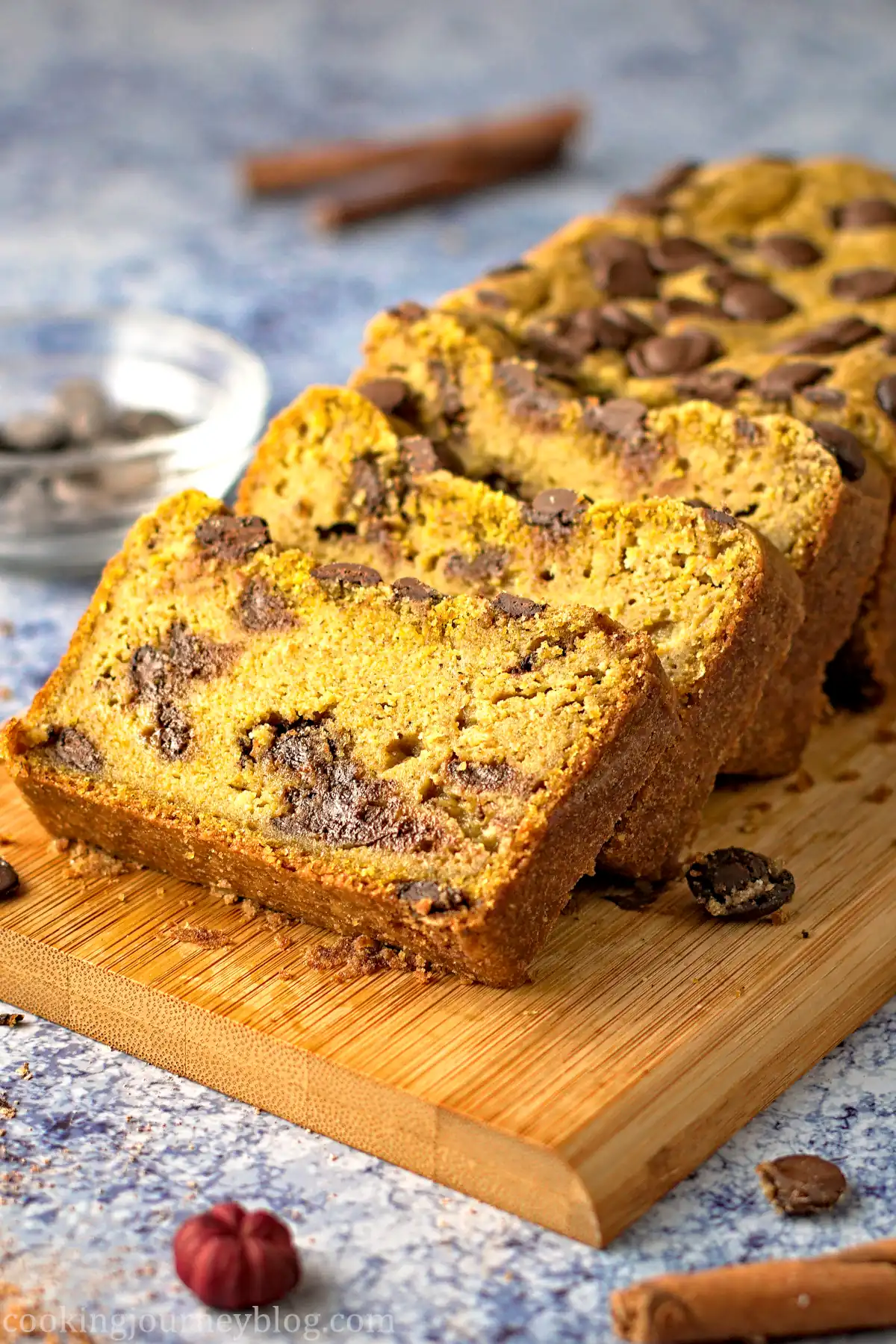Sliced pumpkin chocolate chip bread served on a wooden board with extra chocolate chips.